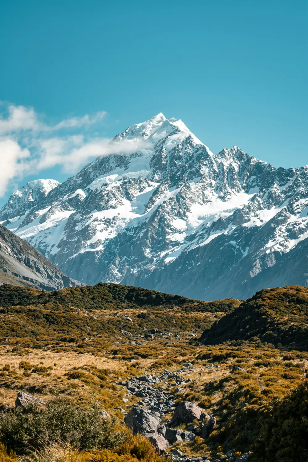 A walker on a valley trail below a snow-capped peak